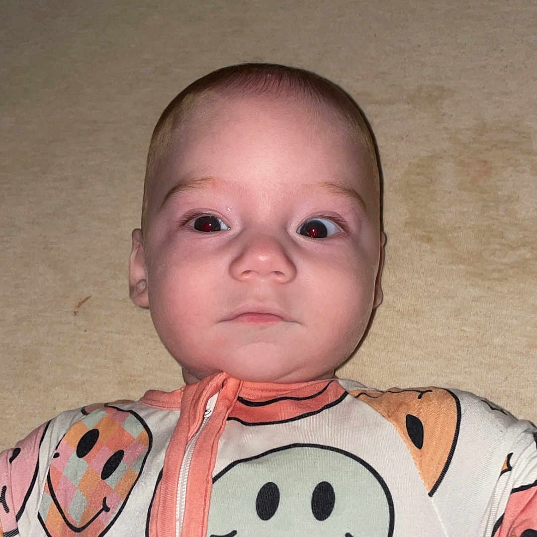 Kai is registered to the contest to win money with this photo: baby, infant, smiley_face, onesie, crib, bed, child, sleepwear, patterned_clothing, indoor, person, face, looking_up, cute, young_child, apparel, baby_clothes, expression, head, lying_down