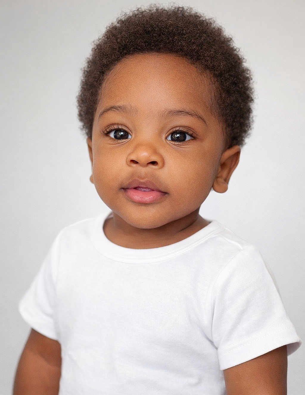 Kaiden is registered to the contest to win money with this photo: toddler, child, portrait, curly_hair, white_tshirt, face, eyes, skin, innocence, expression, young_child, person, head, cute, studio_light, background, photography, closeup, smile, baby