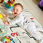 Ezio a rejoint le concours — aidez-le/la à gagner de superbes lots ! baby, infant, play_mat, toy, colorful, smiling, happy, child, onesie, floor, indoors, laughter, cute, bright, playtime, person, young_child, lying_down, joyful, soft_lighting