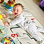 baby, infant, play_mat, toy, colorful, smiling, happy, child, onesie, floor, indoors, laughter, cute, bright, playtime, person, young_child, lying_down, joyful, soft_lighting