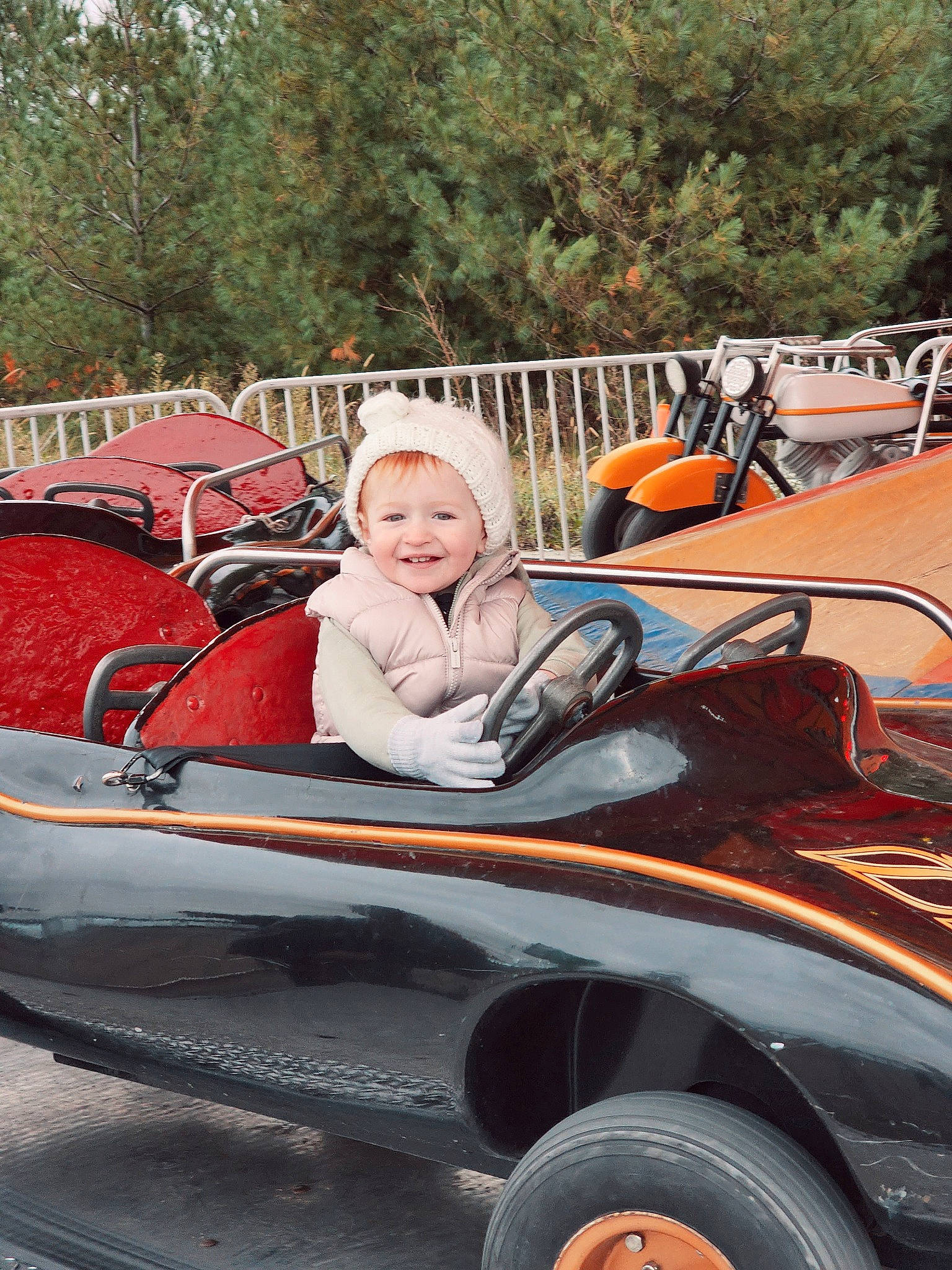 Emarie is registered to the contest to win money with this photo: auto_part, automotive_design, automotive_exterior, automotive_tire, automotive_wheel_system, bumper, helmet, hood, jacket, joy, leisure, motor_vehicle, person, recreation, smile, tire, toddler, tree, vehicle, vehicle_door