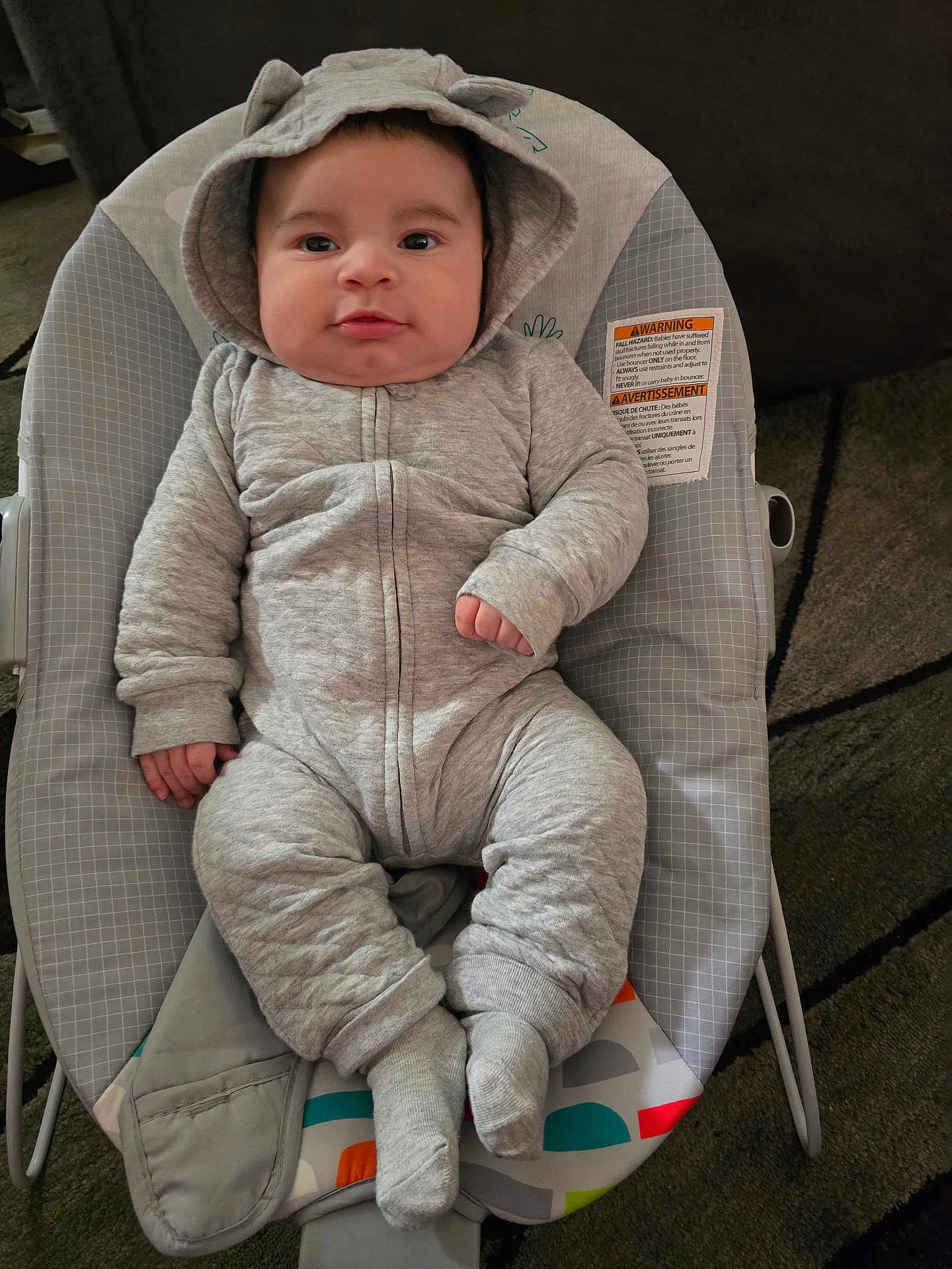 Sebastian joined the competition — help win amazing prizes! baby, infant, child, onesie, hood, baby_rocker, gray_clothing, cute, cozy, face, portrait, socks, indoor, soft_lighting, carpet, cushion, warning_label, small_hands, expression, relaxed