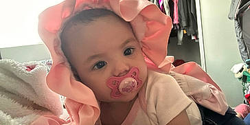 Kaileeanna joined the competition — help win amazing prizes! apparel, baby, bedroom, blanket, child, clothing, cozy, cute, face, headwear, indoor, infant, laying_down, pacifier, person, pink_bonnet, portrait, resting, soft_lighting, toddler