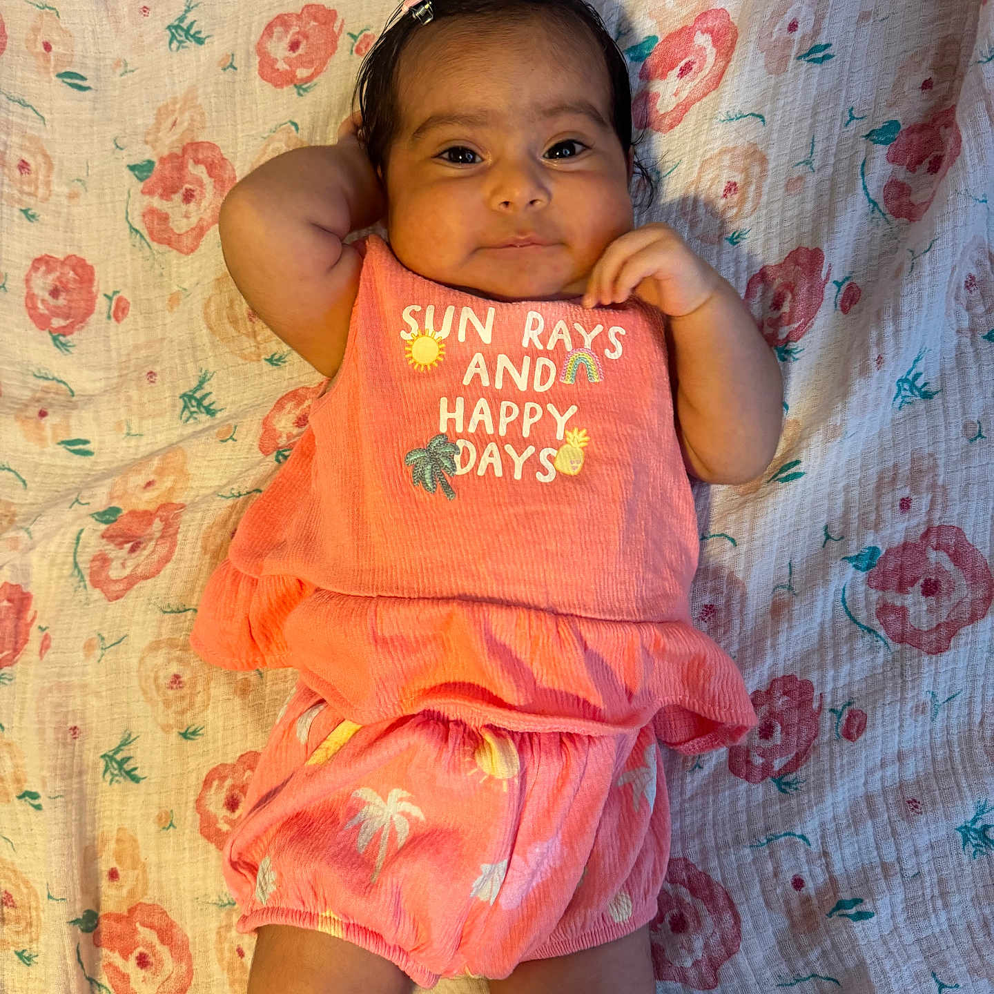 Victoria joined the competition — help win amazing prizes! baby, infant, child, floral_blanket, coral_outfit, smiling, cute, indoors, lying_down, hair_clip, text_on_clothing, skin, legs, arm, hand, fabric, pattern, comfortable, happy, portrait