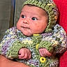 baby, infant, knitted_clothing, hat, sweater, hand, adult_hand, red_shirt, face, portrait, cute, child, warm_clothing, indoor, skin, eyes, expression, holding, newborn, cozy