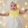 baby, child, infant, dress, yellow, white, bow, headband, daisy_pattern, smile, happy, fairy_lights, soft_texture, cute, portrait, lying_down, adorable, celebration, bright, light