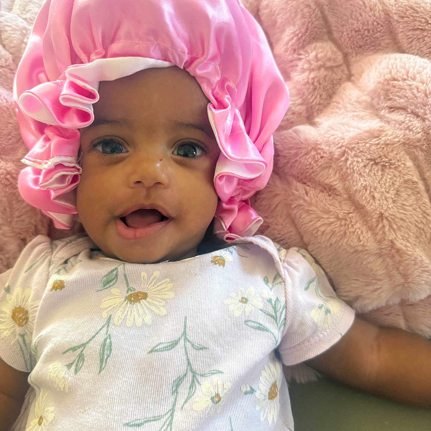 Bella joined the competition — help win amazing prizes! baby, infant, pink_bonnet, floral_onesie, blanket, smile, happy, face, portrait, cute, child, cozy, soft_texture, lying_down, indoors, headwear, apparel, skin, person, expression