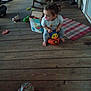 Freya is registered to the contest to win money with this photo: toddler, child, toy, pacifier, wooden_floor, porch, box, rocking_chair, plastic_toy, indoor, clothing, barefoot, hair_tied, floor_mat, furniture, person, playtime, casual, young_child, home