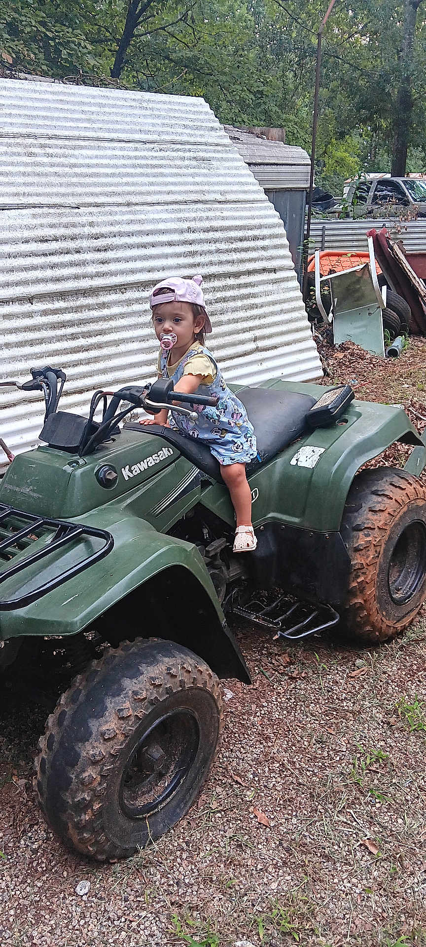 Freya is registered to the contest to win money with this photo: toddler, child, pacifier, hat, atv, kawasaki, outdoor, gravel, rustic, dirt, vehicle, wheel, cap, clothing, nature, trees, person, young_child, play, curious