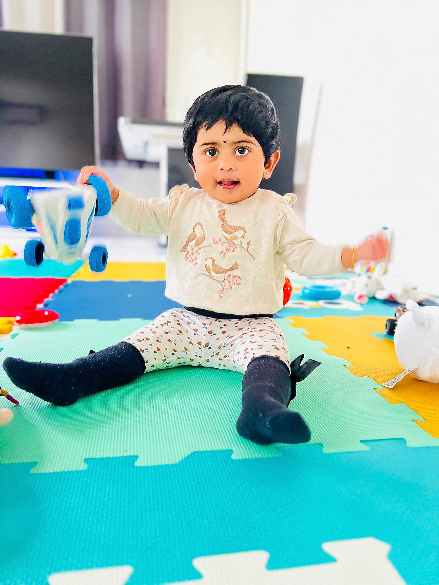 Kiyara participe au concours pour gagner de l'argent avec cette photo : toddler, child, toy, playmat, indoor, smiling, sitting, colorful, car_toy, leggings, socks, long_sleeve_shirt, black_hair, face, young_child, floor, playtime, cute, happy, home