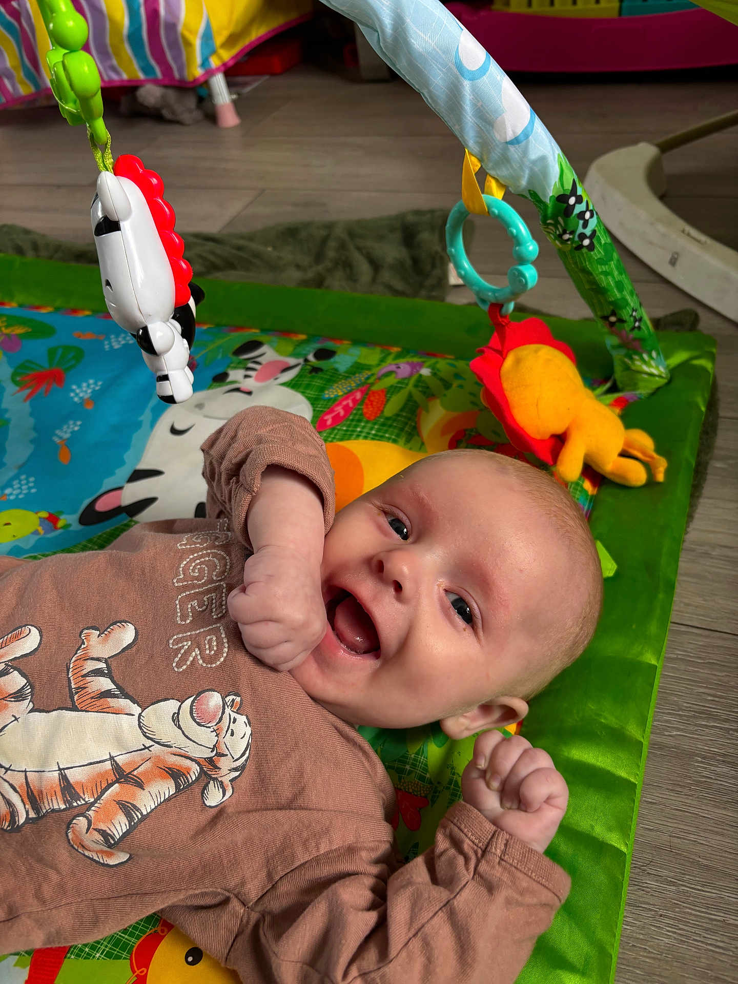 Cody is registered to the contest to win money with this photo: baby, smiling, play_mat, toy, colorful, infant, happy, floor, child, clothing, tiger_print, cute, indoor, young_child, hands_up, face, expression, playtime, bright, casual