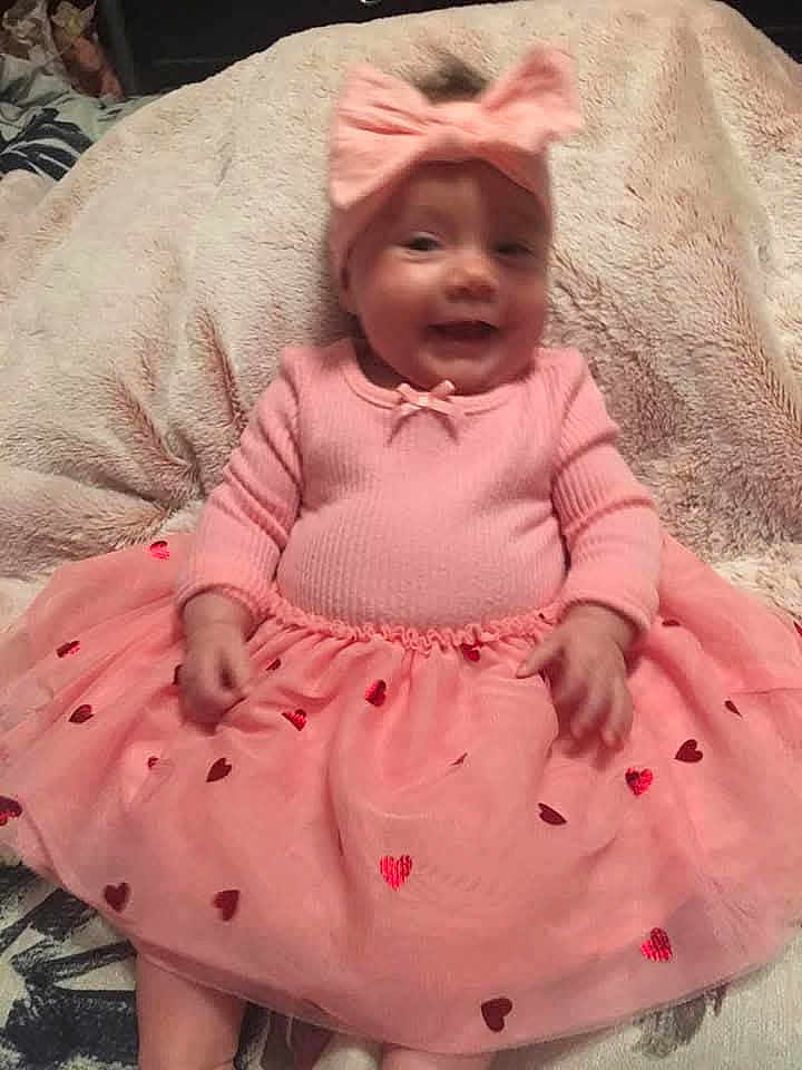 Sophia is registered to the contest to win money with this photo: baby, pink_outfit, bow_headband, smiling, sitting, blanket, heart_patterns, cute, infant, happy, soft_texture, indoors, child, portrait, tutu_skirt, adorable, young_child, headwear, hands, cozy