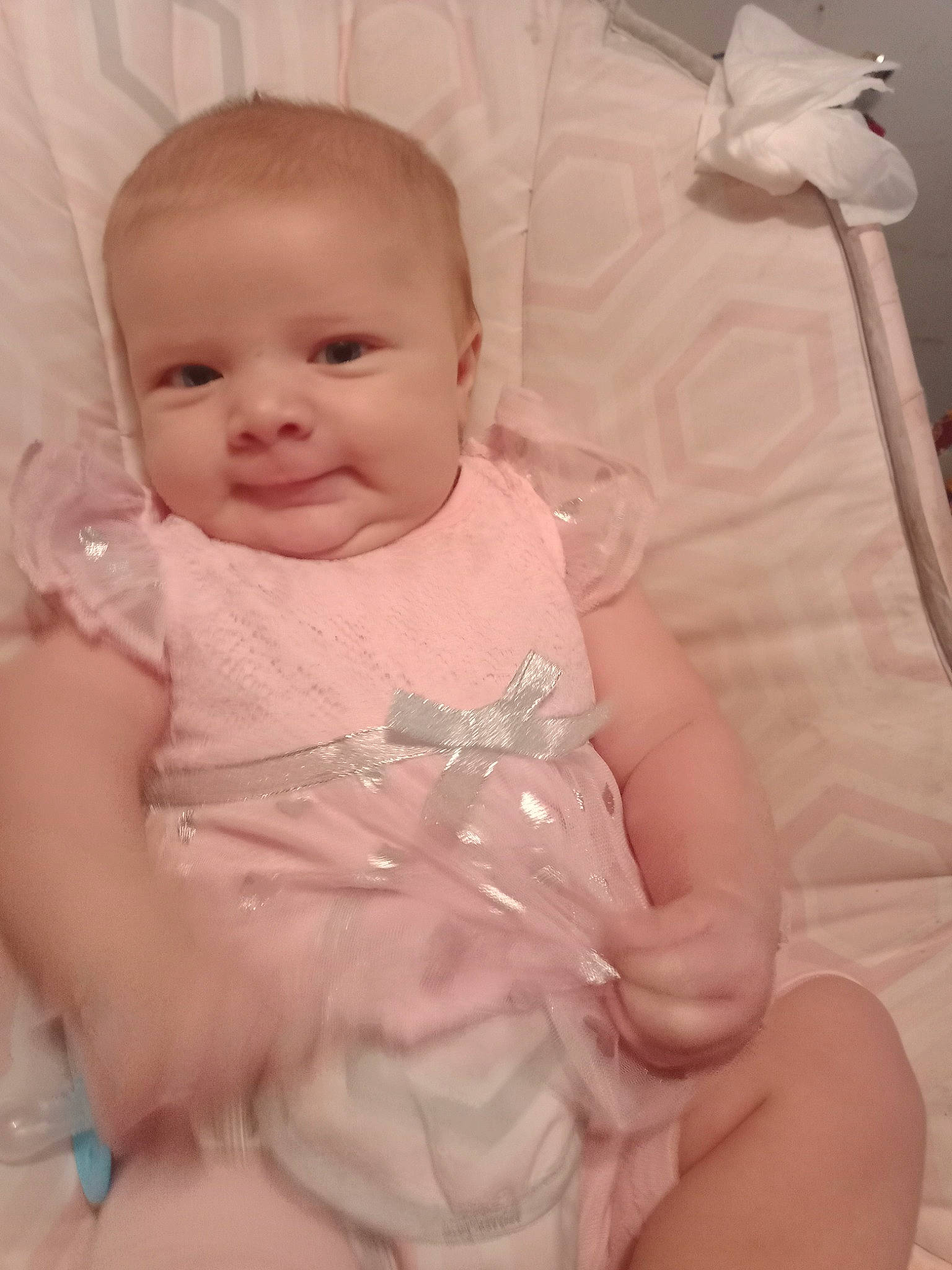 Raelyn is registered to the contest to win money with this photo: abdomen, baby, baby_products, baby_toddler_clothing, cheek, child, comfort, dress, eye, finger, happy, iris, lip, person, pink, room, sitting, skin, sleeve, smile