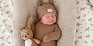 Oscar is registered to the contest to win money with this photo: baby, sleeping, plush_toy, knitted_hat, brown_outfit, cushion, bed, blanket, soft_toys, infant, cozy, nursery, child, cute, indoor, peaceful, resting, knitwear, toddler, portrait