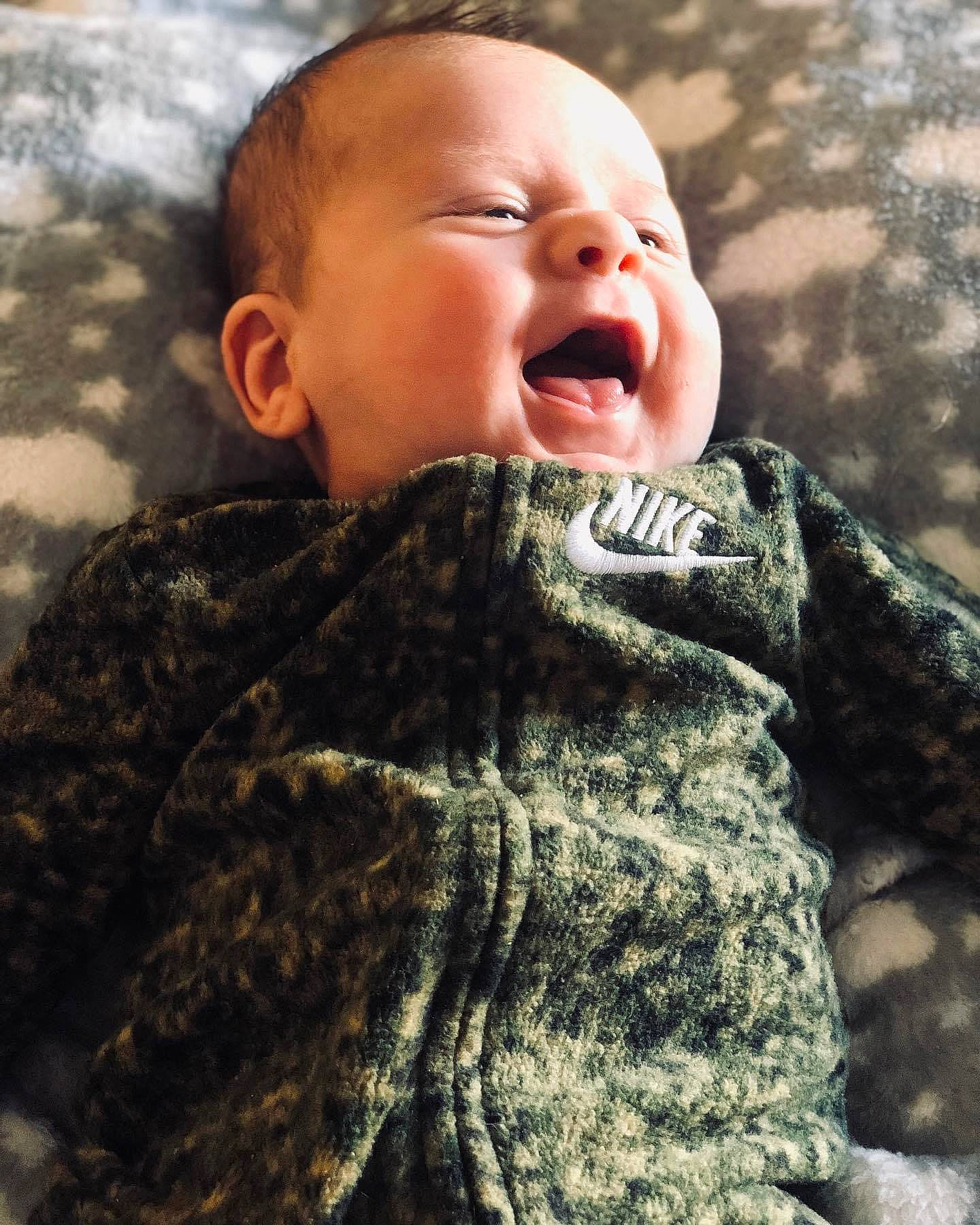 Michael is registered to the contest to win money with this photo: baby, baby_toddler_clothing, cheek, child, comfort, face, gesture, grass, happy, military_camouflage, outerwear, pattern, people_in_nature, person, skin, sleeve, smile, textile, toddler, wool