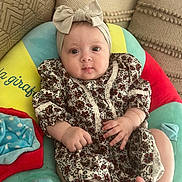 Rania a rejoint le concours — aidez-le/la à gagner de superbes lots ! baby, infant, headband, bow, dress, floral_pattern, cushion, colorful, hand, foot, face, eyes, indoors, comfort, cute, child, patterned_clothing, soft_toy, pillow, relaxation