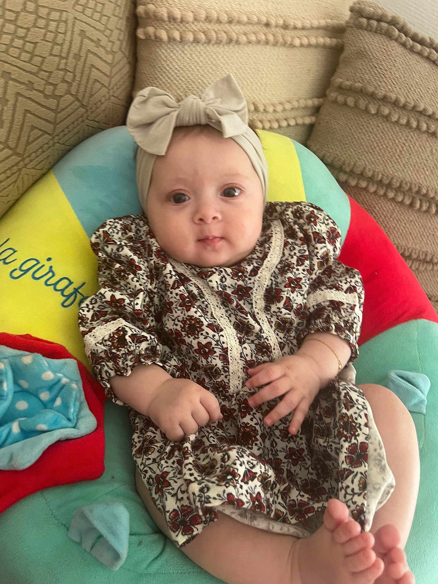 Rania a rejoint le concours — aidez-le/la à gagner de superbes lots ! baby, infant, headband, bow, dress, floral_pattern, cushion, colorful, hand, foot, face, eyes, indoors, comfort, cute, child, patterned_clothing, soft_toy, pillow, relaxation