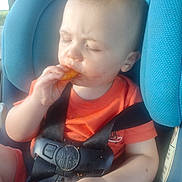 Christian joined the competition — help win amazing prizes! baby, child, car_seat, orange_shirt, snack, messy_face, black_harness, seatbelt, closed_eyes, eating, hand, car, window, seat, infant, young_child, cute, food, mess, portrait
