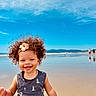 beach, child, clouds, curly_hair, happy, headband, mountains, ocean, outdoor, person, reflection, sand, seashells, sky, smiling, summer, sunny, toddler, vacation, water