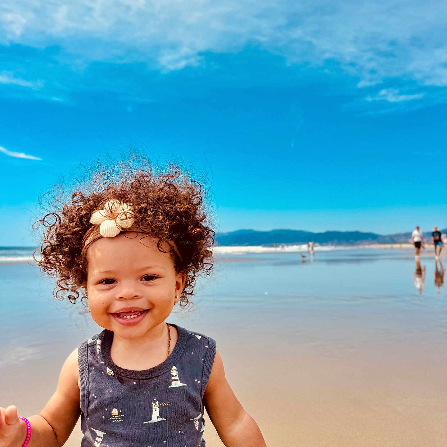 Aracely joined the competition — help win amazing prizes! beach, child, clouds, curly_hair, happy, headband, mountains, ocean, outdoor, person, reflection, sand, seashells, sky, smiling, summer, sunny, toddler, vacation, water