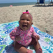 Naailah is registered to the contest to win money with this photo: baby, smiling, beach, towel, sand, umbrella, sunny, headband, pink, floral, child, happy, summer, outdoor, feet, sitting, ocean, blue, vacation, person