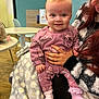 Daisy is registered to the contest to win money with this photo: baby, child, person, smile, pink_outfit, blanket, hand, indoor, table, chair, floor, wall, hair, furniture, socks, happy, holding, pattern, clothing, cute