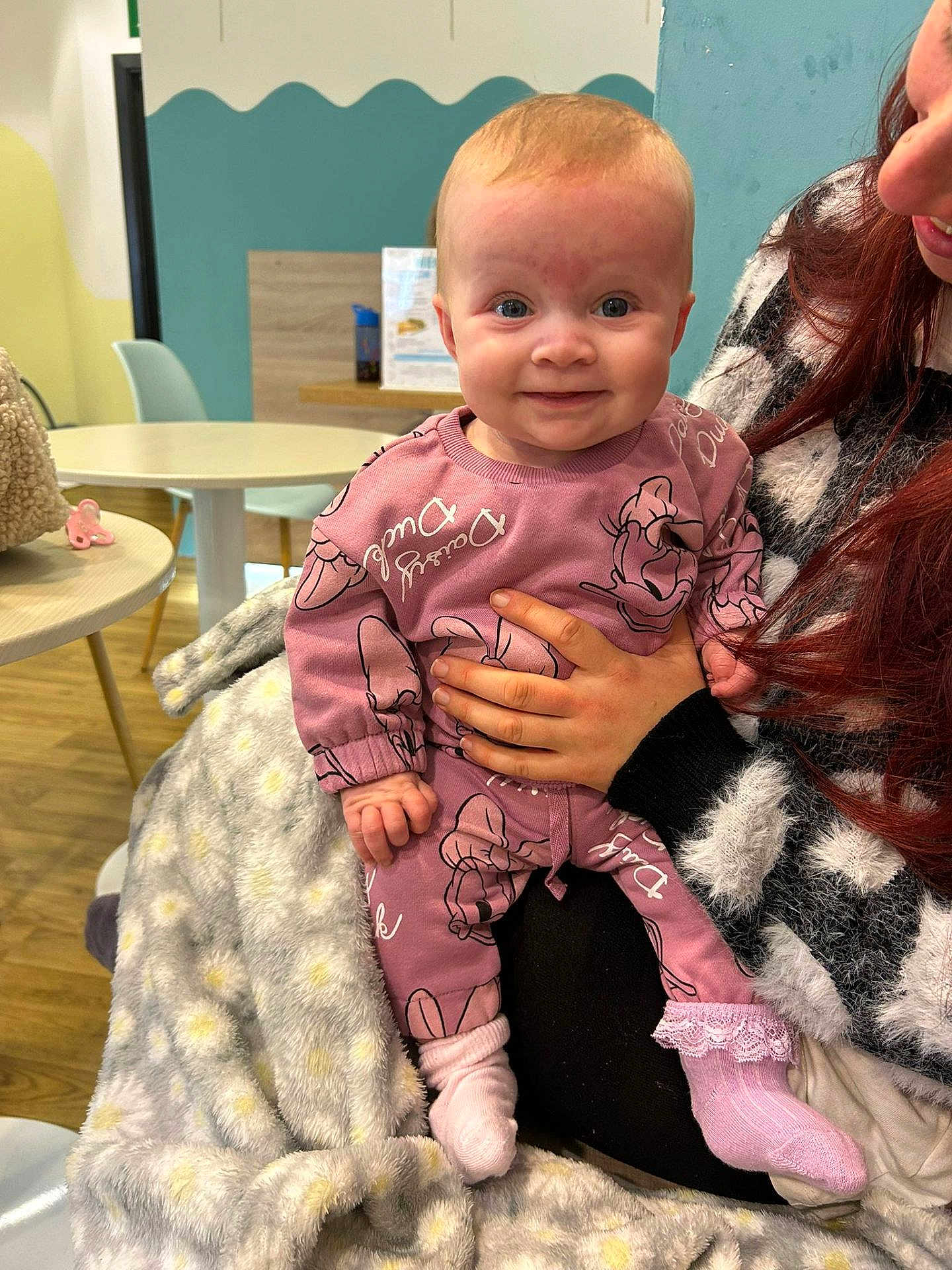 Daisy is registered to the contest to win money with this photo: baby, child, person, smile, pink_outfit, blanket, hand, indoor, table, chair, floor, wall, hair, furniture, socks, happy, holding, pattern, clothing, cute