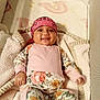 Hazel is registered to the contest to win money with this photo: baby, smiling, infant, floral_clothing, pink_bandana, blanket, crib, soft, cute, happy, child, indoors, sleeping_area, babywear, toddler, person, face, hand, head, lying_down