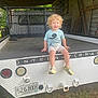 Ryder joined the competition — help win amazing prizes! child, toddler, curly_hair, smiling, tshirt, shorts, shoes, truck, license_plate, metal, wood, rustic, outdoor, grass, daylight, vehicle, back_of_truck, farm_equipment, sitting, happy