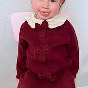 Camélia a rejoint le concours — aidez-le/la à gagner de superbes lots ! child, girl, toddler, smile, gap_tooth, hair_bow, maroon_outfit, sweater, skirt, pink_chair, sitting, portrait, earrings, indoor, happy, legs, knee_socks, pale_skin, wall_background, cute