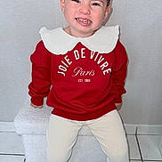 Camélia participe au concours pour gagner de l'argent avec cette photo : child, toddler, girl, smiling, red_sweatshirt, white_collar, hair_bun, earrings, sitting, indoor, tiled_floor, slippers, cream_leggings, bench, portrait, eyes, teeth, wall, clothing, happy