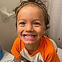 child, smile, happy, hairband, orange_shirt, bathroom, counter, toiletries, toilet, face, person, young_child, portrait, cute, expression, indoor, playful, curly_hair, teeth, closeup