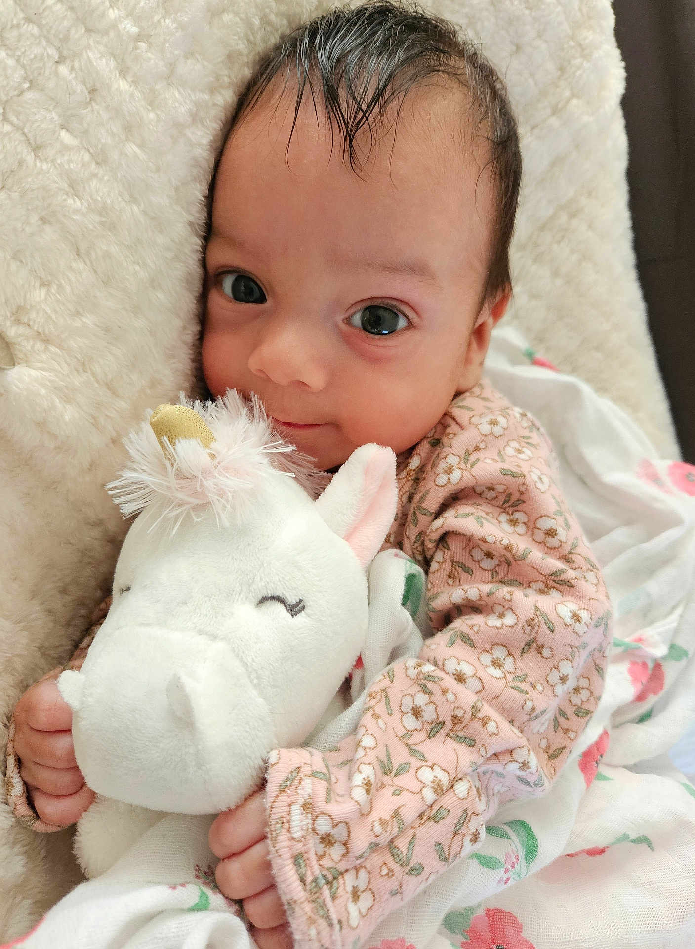Irene is registered to the contest to win money with this photo: baby, infant, child, plush_toy, unicorn, blanket, floral_pattern, pink_clothing, cute, smiling, soft_texture, closeup, indoors, person, portrait, toddler, cozy, sleepytime, hand, face