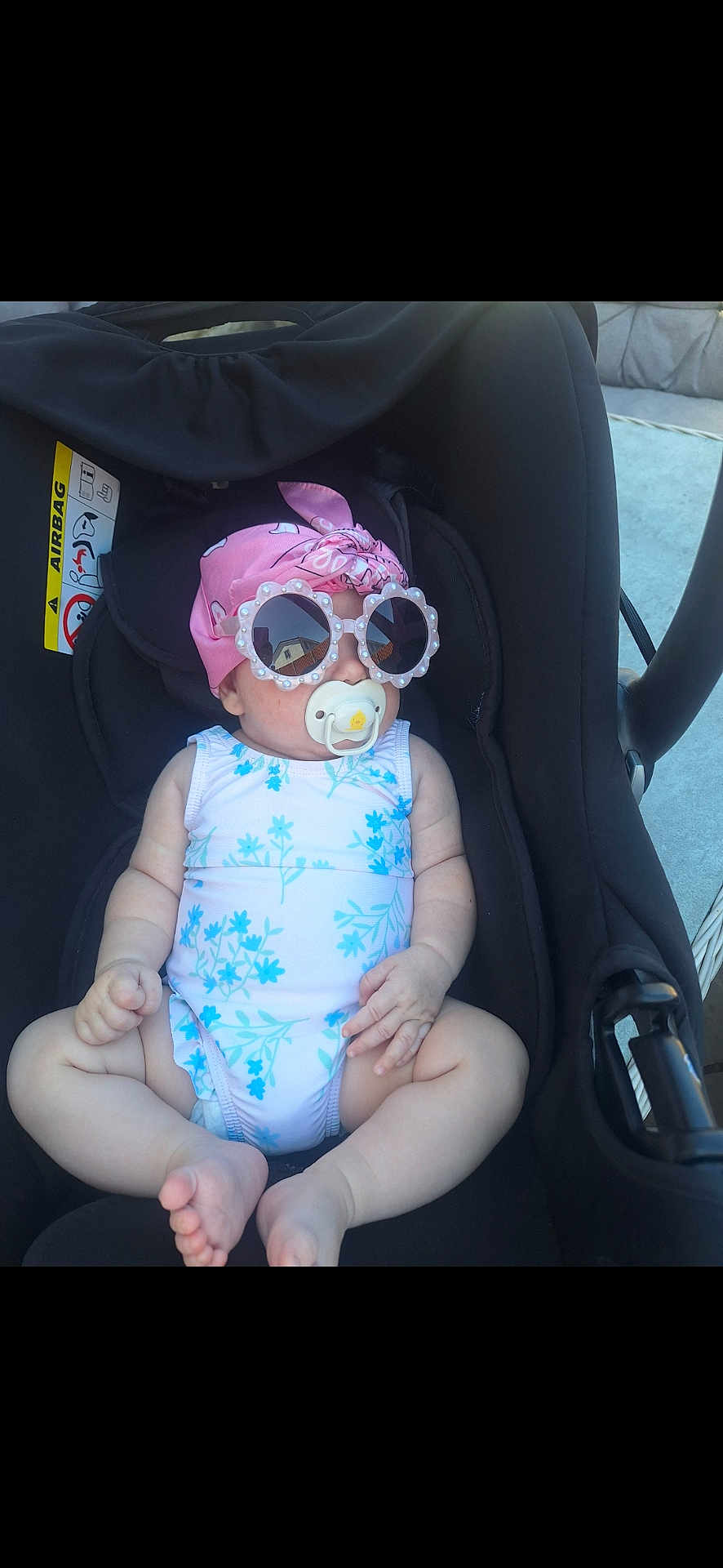 Bella Marie is registered to the contest to win money with this photo: baby, car_seat, sunglasses, pacifier, headscarf, pink, blue, white, floral_pattern, infant, child, outdoor, sunny, cute, relaxed, clothing, seat, accessory, portrait, person