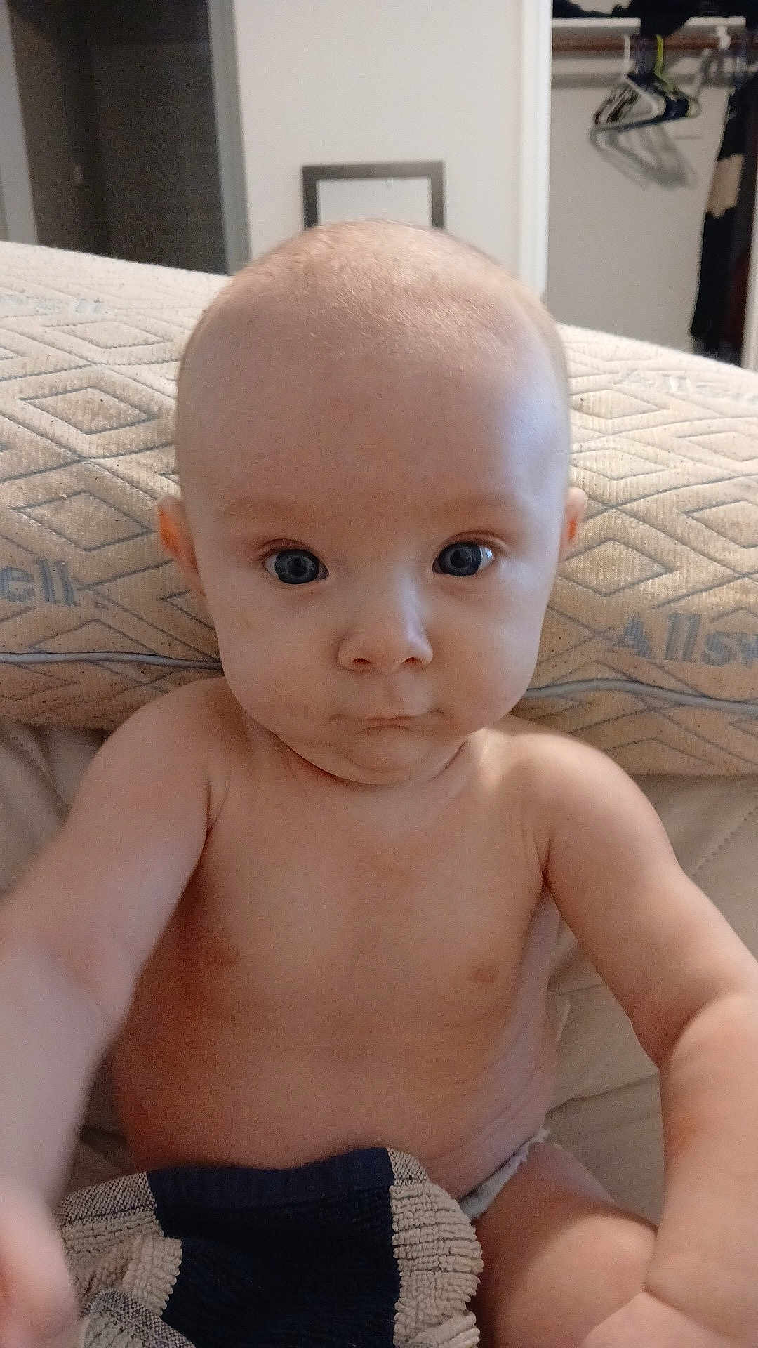 Arthur is registered to the contest to win money with this photo: baby, infant, child, face, eyes, blue_eyes, bald_head, bare_chest, blanket, mattress, pillow, diaper, bed, indoor, portrait, close_up, sitting, curious, expression, soft_lighting