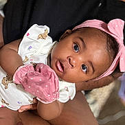 Azeria is registered to the contest to win money with this photo: baby, infant, headband, pink, mittens, person, cute, tattoo, arm, clothing, portrait, curious, indoor, holding, closeup, child, skin, face, expression, blurred_background