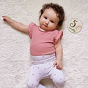 Gemma participe au concours pour gagner de l'argent avec cette photo : baby, infant, child, pink_clothing, curly_hair, milestone_marker, 5_months, white_rug, soft_texture, lying_down, cute, sock, patterned_pants, portrait, indoors, smiling, skin, person, young_child, relaxed