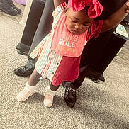 Makayla joined the competition — help win amazing prizes! toddler, child, baby, red_bow, colorful_clothing, pink_bib, shoes, carpet, indoor, person, adult_hands, floor, home, standing, holding_hands, cute, fashion, playful, learning_to_walk, support