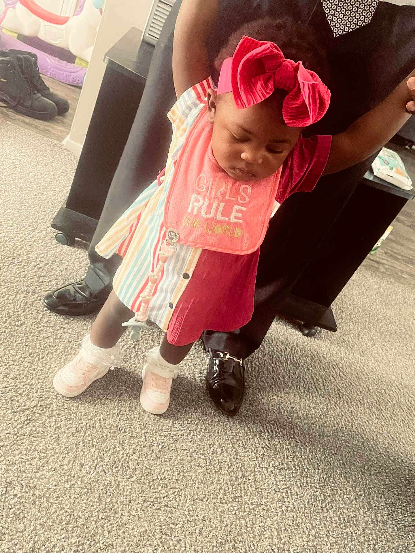 Makayla joined the competition — help win amazing prizes! toddler, child, baby, red_bow, colorful_clothing, pink_bib, shoes, carpet, indoor, person, adult_hands, floor, home, standing, holding_hands, cute, fashion, playful, learning_to_walk, support