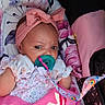 baby, baby_gear, baby_seat, blanket, calm, child, close_up, colorful, eyes_open, face, floral_clothing, headband, indoors, infant, pacifier, photograph, pink_bow, portrait, sitting, toy_strap