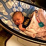 baby, bassinet, bedtime, black_shirt, blanket, clothing, cozy, crib, face, indoor, infant, newborn, nursery, pacifier, patterned_bedding, pink_blanket, portrait, resting, sleeping, warm_lighting
