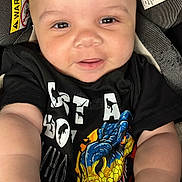 Omari is registered to the contest to win money with this photo: baby, child, smiling, face, tshirt, dinosaur, car_seat, warning_label, infant, hand, cute, portrait, young_child, clothing, seatbelt, indoor, person, closeup, happy, skin