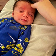 Rimington is registered to the contest to win money with this photo: baby, infant, newborn, smiling, sleeping, face, closed_eyes, hand_touching, onesie, blue_clothing, nike_swoosh, pillow, bedding, blanket, indoor, portrait, close_up, soft_lighting, cute, peaceful