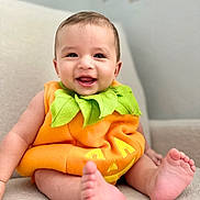 Noah is registered to the contest to win money with this photo: baby, infant, pumpkin_costume, smiling, happy, cute, child, feet, orange, green, clothing, costume, portrait, indoors, soft_surface, head, face, eyes, mouth, skin