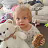 April is registered to the contest to win money with this photo: toddler, child, teddy_bear, toy, granola_bar, couch, cat, blanket, living_room, furniture, floor, clothing, hair, face, person, indoor, snack, plush, pet, messy