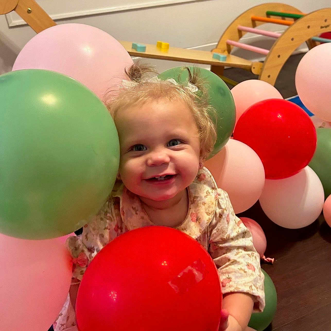 April joined the competition — help win amazing prizes! toddler, child, balloon, red_balloon, pink_balloon, green_balloon, indoor, smile, happy, cute, hair_pigtails, wooden_furniture, floor, playroom, window, light, celebration, colorful, portrait, clothing