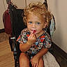 April is registered to the contest to win money with this photo: child, toddler, stroller, lollipop, curly_hair, blue_eyes, indoor, shirt, harley_davidson, towel, purse, floor, wood_floor, cabinet, person, sitting, cute, snack, curious, baby