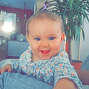 Alba a rejoint le concours — aidez-le/la à gagner de superbes lots ! baby, child, smile, happy, indoor, plant, couch, hand, face, person, home, furniture, living_room, clothing, blue_eyes, hair_tie, patterned_shirt, curly_hair, cute, portrait