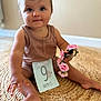 baby, child, infant, sitting, milestone_card, pink_flowers, brown_outfit, woven_rug, cute, portrait, indoor, smiling, person, hand, foot, head, face, blue_eyes, decor, soft_lighting