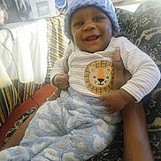 Hezekiah joined the competition — help win amazing prizes! baby, child, smile, happy, hat, knitted_hat, cozy_clothing, striped_shirt, patterned_pants, hand, adult_hand, couch, furniture, indoor, portrait, person, infant, warm_clothing, blanket, room